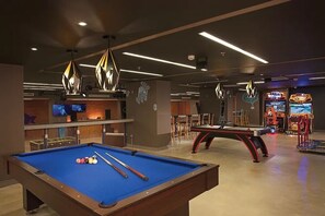 A pool table with billiard balls and cues, a bar area with a TV, and arcade games in a dimly lit room. - Luxury, Ocean view room at Dreams Playa Mujeres (Quintana Roo)