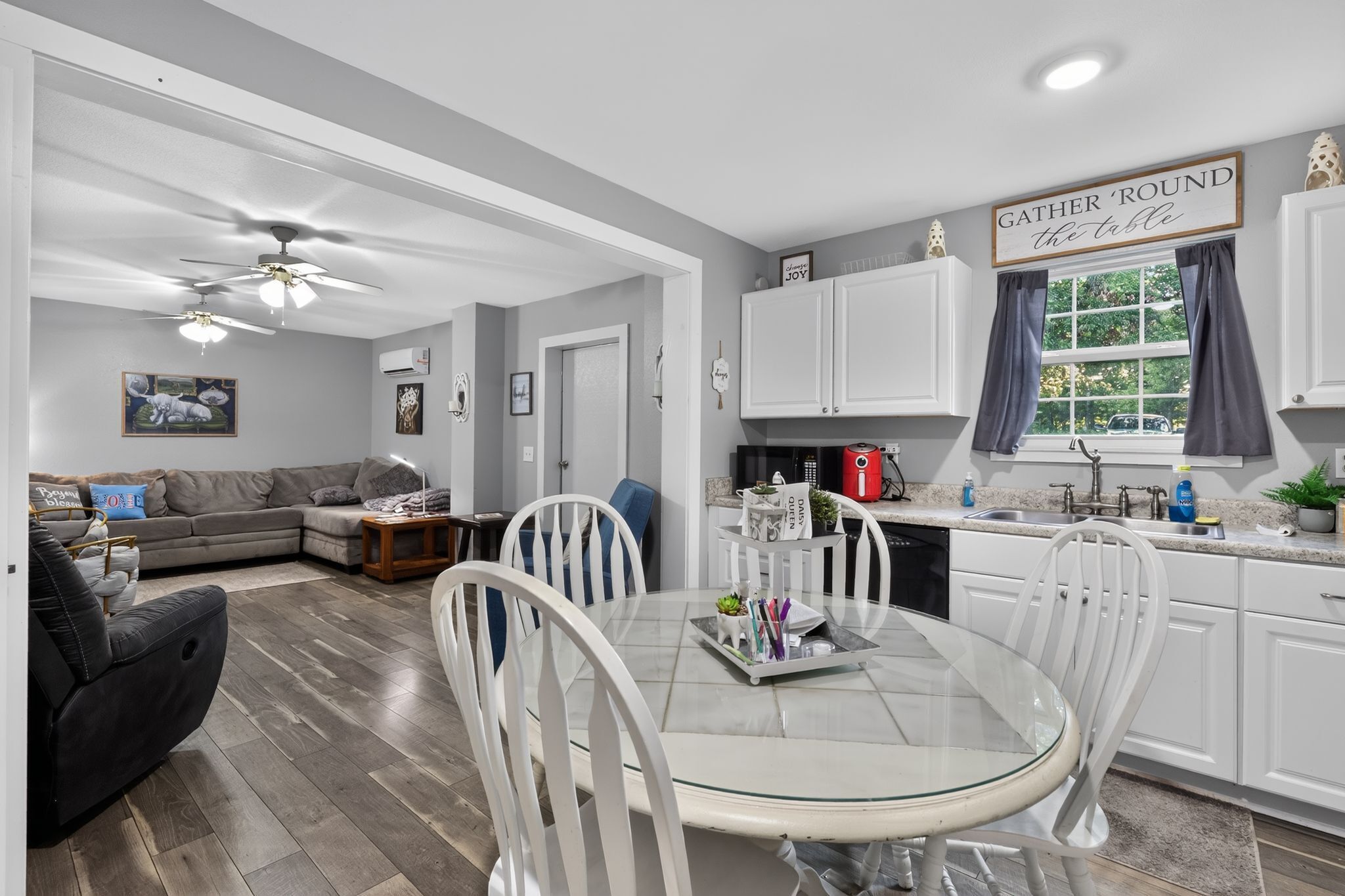 A modern kitchen with white cabinets, a dining table with chairs, and a ceiling fan.