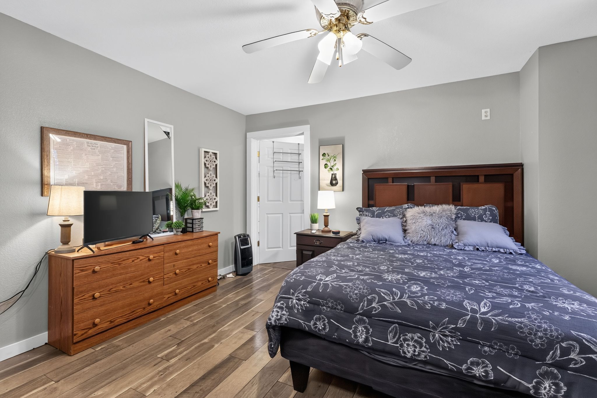 A bedroom with a bed, dresser, television, and ceiling fan.