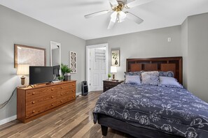 A bedroom with a bed, dresser, television, and ceiling fan.