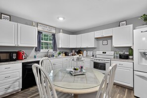 A modern kitchen with white cabinets, a glass dining table, and various appliances including a microwave, coffee maker, and stove.