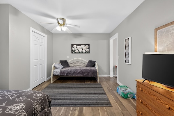 A bedroom with a bed, a ceiling fan, a television, and a framed picture on the wall.