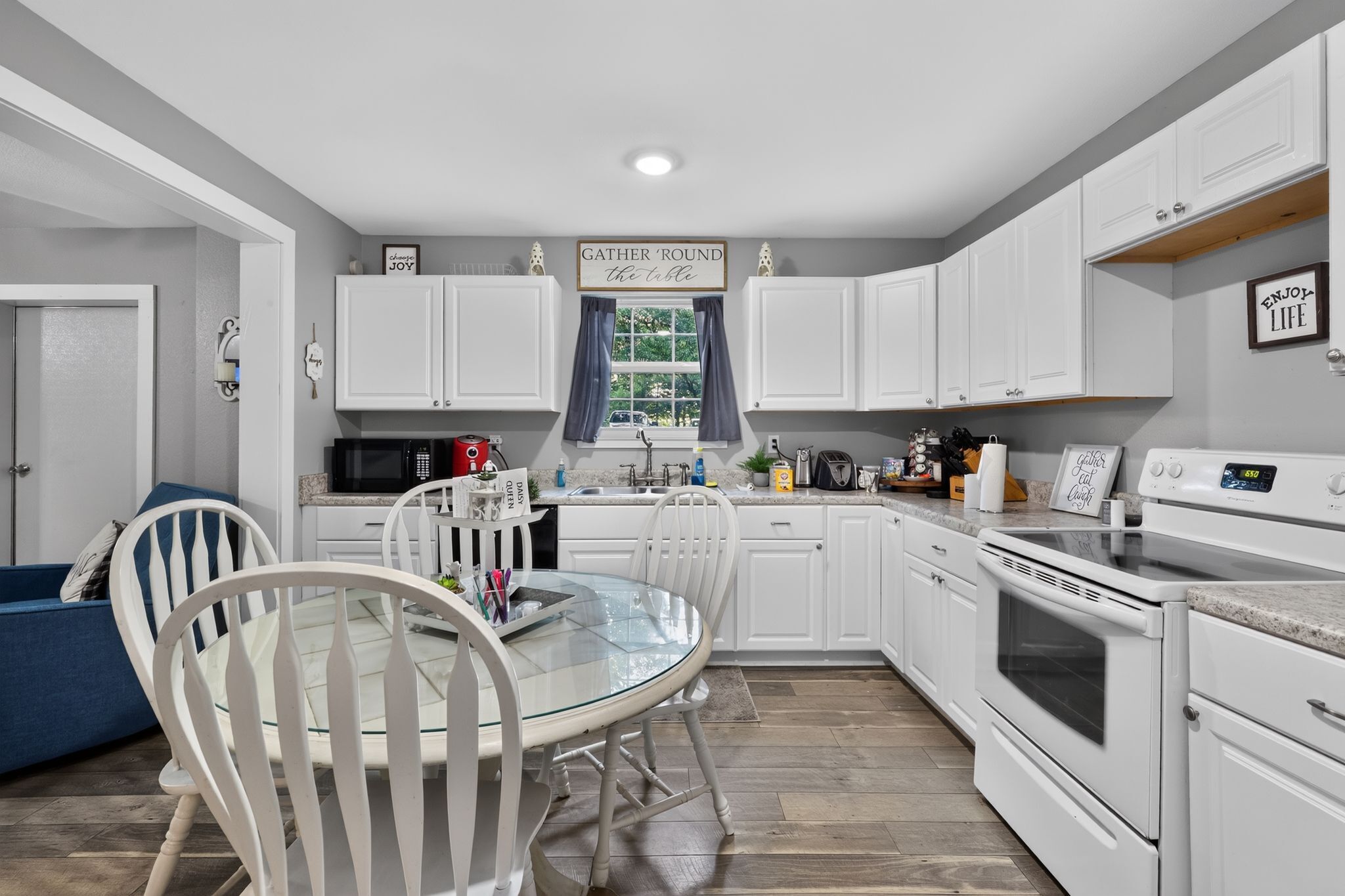 A modern kitchen with white cabinets, a round glass table, and a dining area with white chairs.