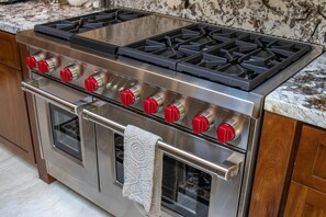 Um fogão de aço inoxidável com fogão a gás e forno, com botões vermelhos e uma toalha pendurada na maçaneta do forno.