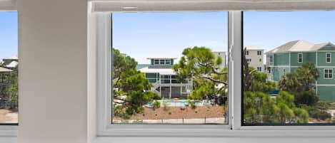 A window with a view of a building with a green roof and white walls, surrounded by trees.