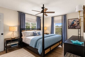 Ein Schlafzimmer mit einem Himmelbett, einem Deckenventilator und Blick ins Freie durch große Fenster.