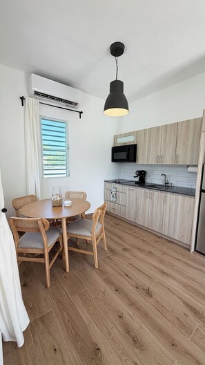 A compact kitchen with a dining area, featuring a round table, chairs, and a hanging light fixture. - Beach Lote Villas - Villa 1 +Pool-  Islote (Arecibo)