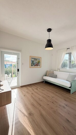 A room with a wooden floor, a white sofa, a black pendant light, and a painting on the wall. - Beach Lote Villas - Villa 1 +Pool-  Islote (Arecibo)