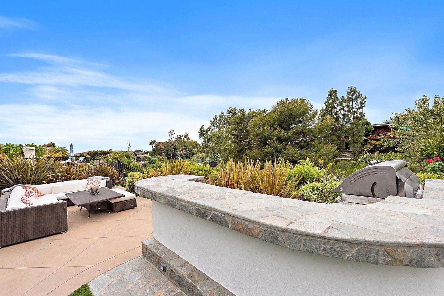 An outdoor patio area with a stone bench, a grill, and a seating area with cushions.