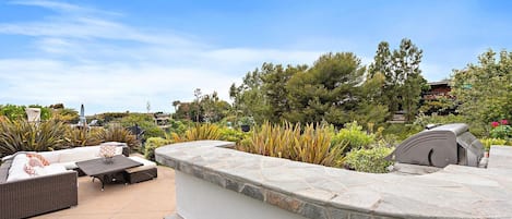 An outdoor patio area with a stone bench, a grill, and a seating area with cushions.