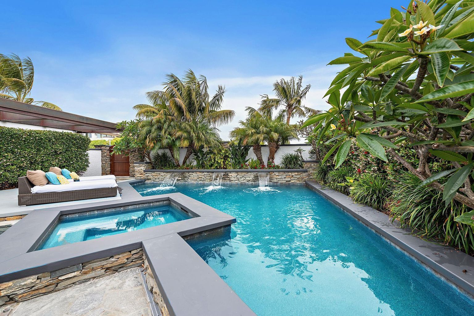 A swimming pool with a waterfall feature, surrounded by lush greenery and a stone wall.