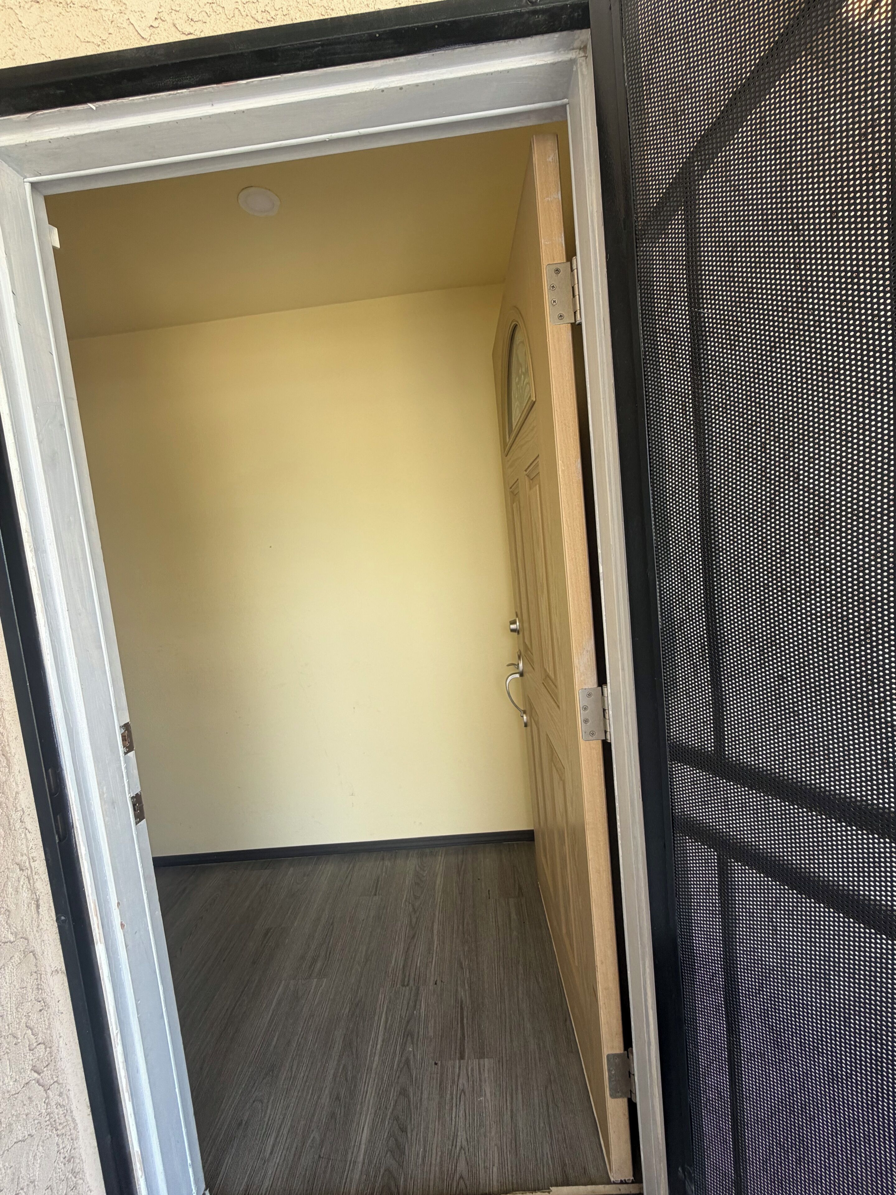 Puerta abierta que da a un espacio con marco de madera, pared con textura y suelo de madera oscura.