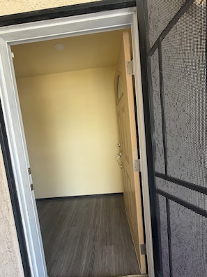 Une porte ouverte donne sur une pièce dont l’encadrement est en bois, dont le mur présente une texture particulière et dont le plancher est en bois foncé.