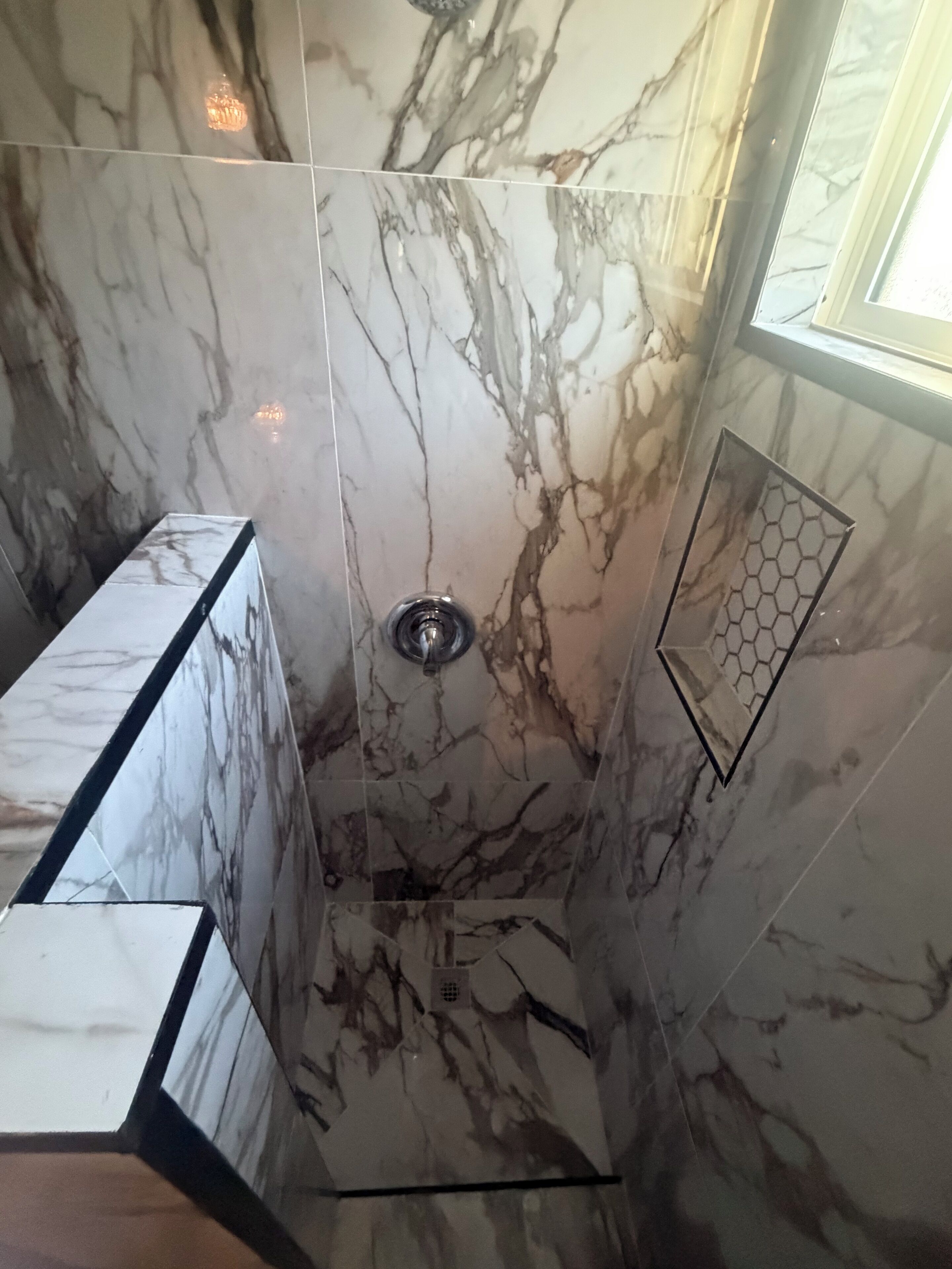A bathroom with marble walls, a shower area, and a window.