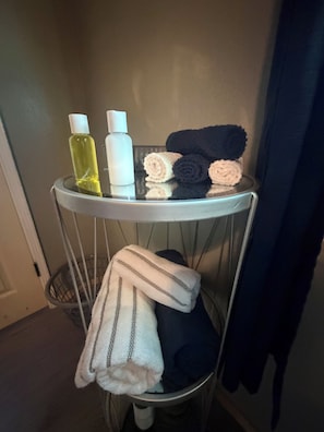 Une petite étagère en métal où sont rangés des articles de toilette, des serviettes et une veste.