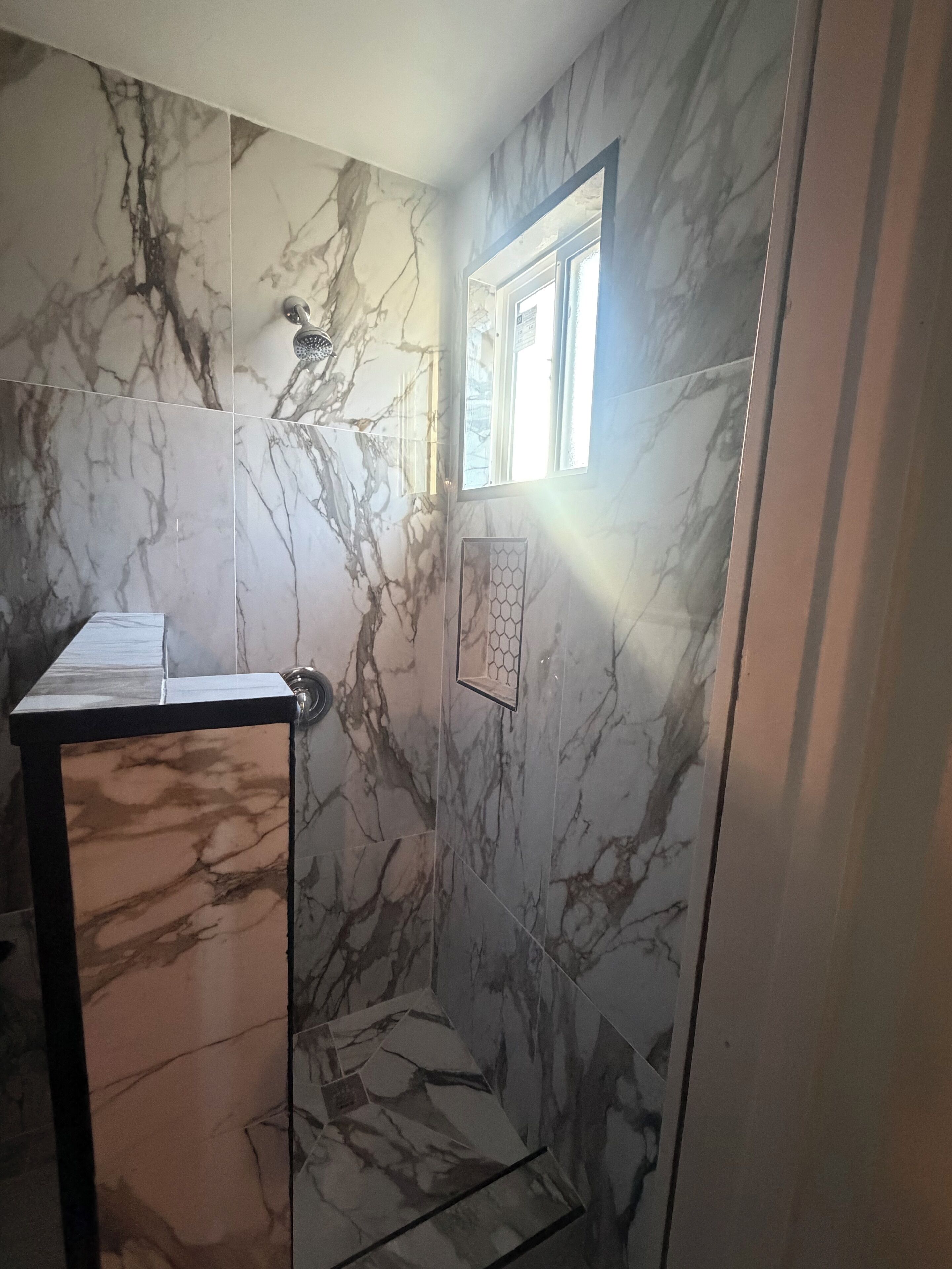 Un baño con paredes de mármol, una ducha y un ventanal.