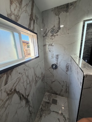 Un baño con paredes de mármol, ducha y ventana.