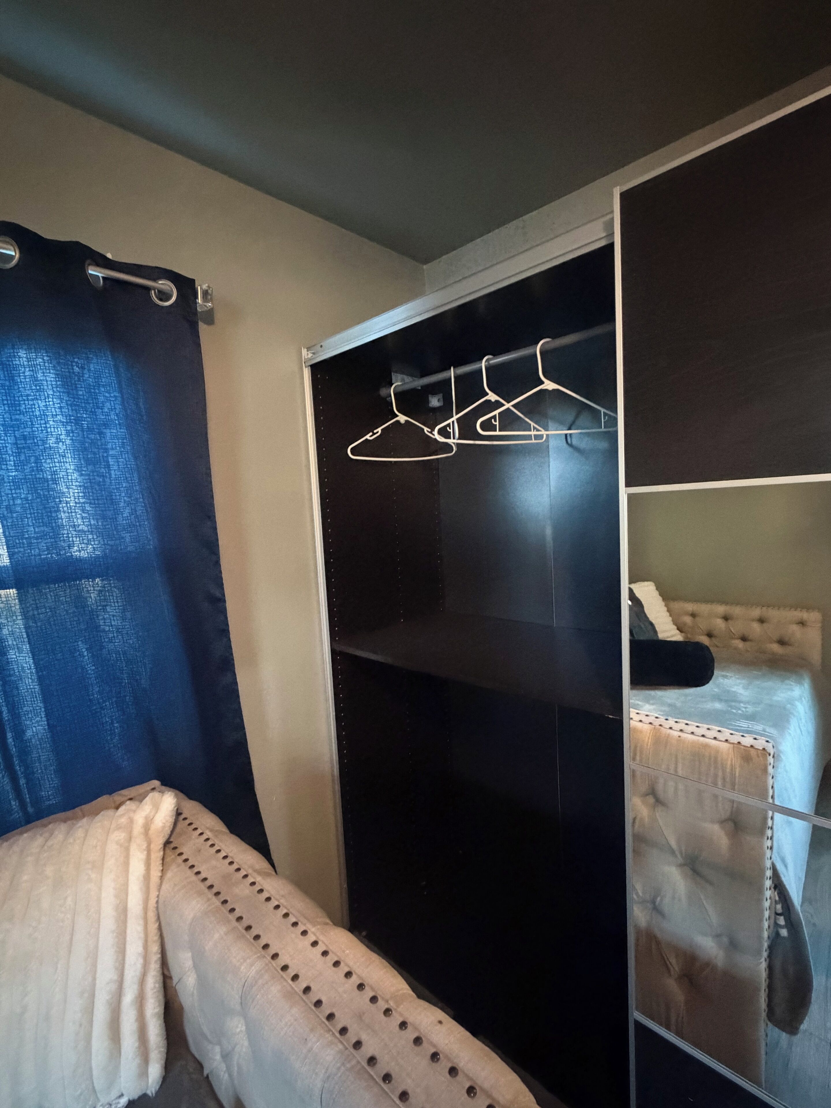A bedroom with a bed, a wardrobe, and a hanging clothes rack.