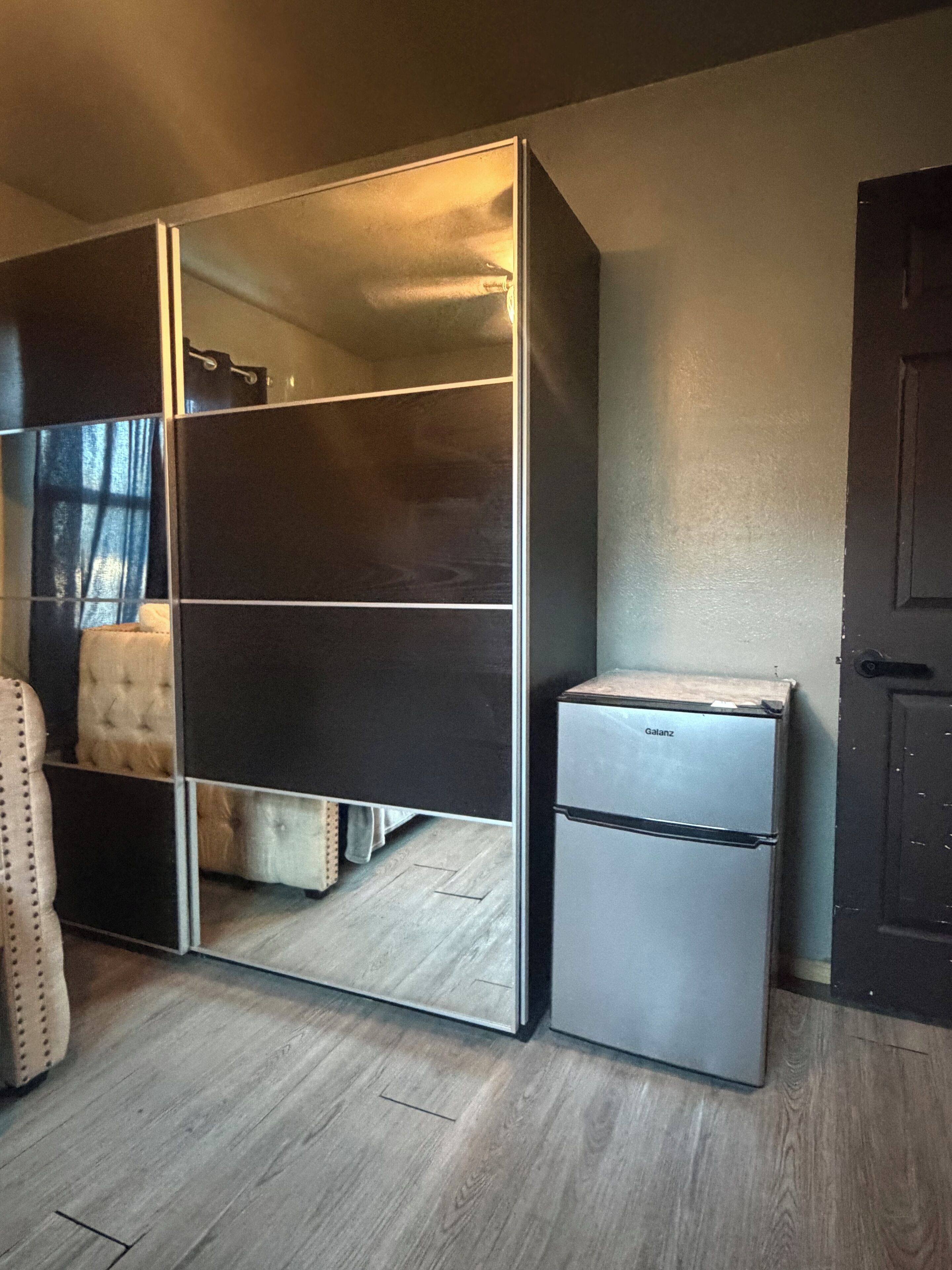 Una habitación compacta con armario, refrigerador pequeño y cama con cabecera.