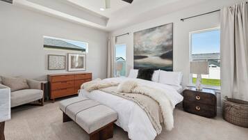 A bedroom with a bed, a bench, a dresser, a lamp, and a large window with a view.