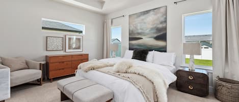 A bedroom with a bed, a bench, a dresser, a lamp, and a large window with a view.
