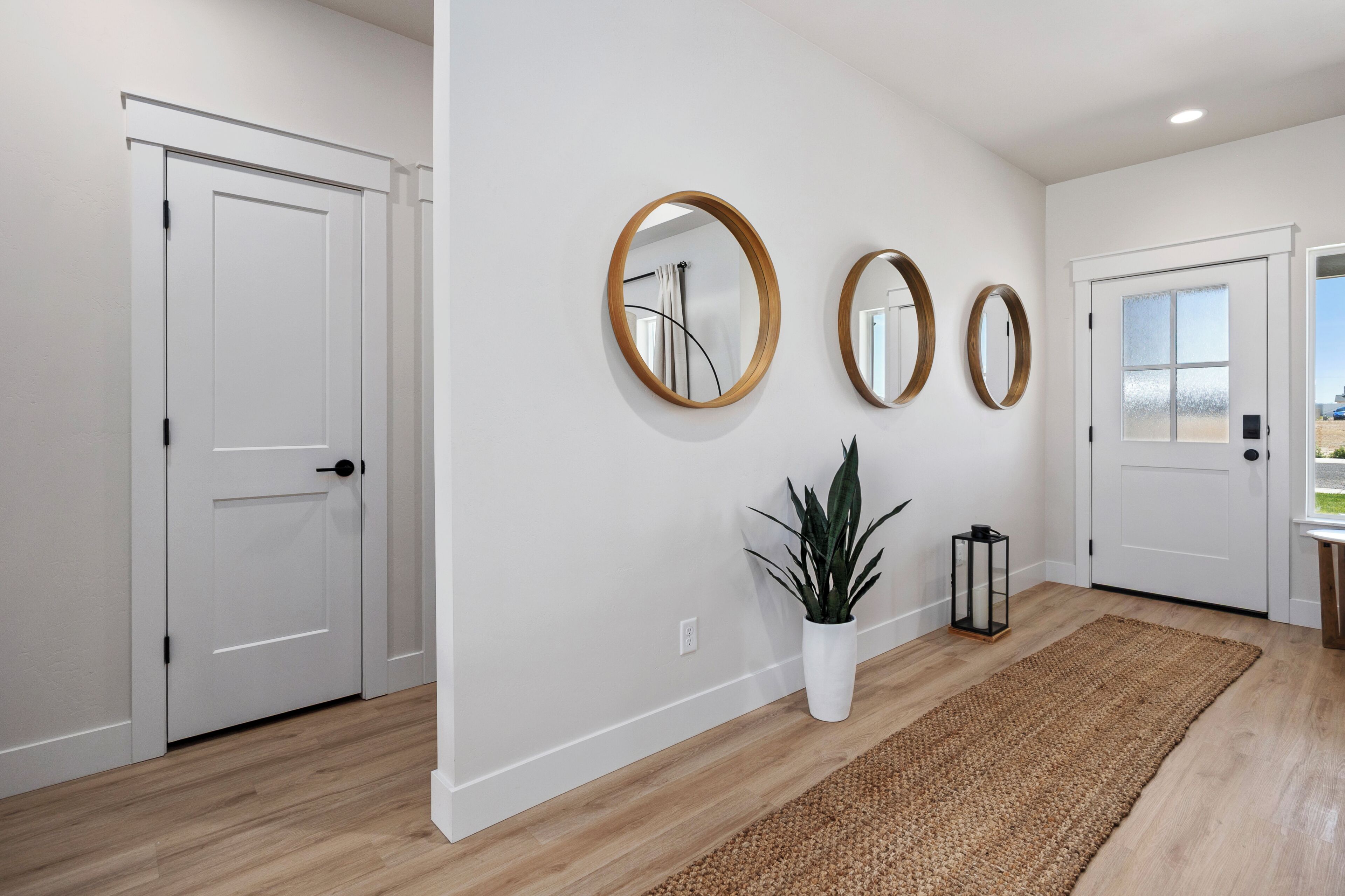Un couloir aux murs blancs, au sol en bois, et orné de trois miroirs ronds accrochés au mur.