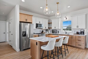Una cocina moderna con electrodomésticos de acero inoxidable, armarios blancos y una isla central con taburetes de bar.