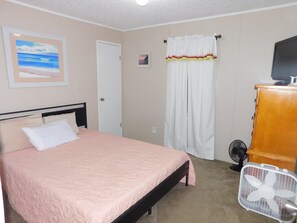 Ein Schlafzimmer mit einem Bett, einem Ventilator, einem Holzschrank und einem Bild an der Wand.