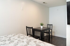 Habitació petita i ben il·luminada amb un llit, una taula amb cadires i una planta en test.