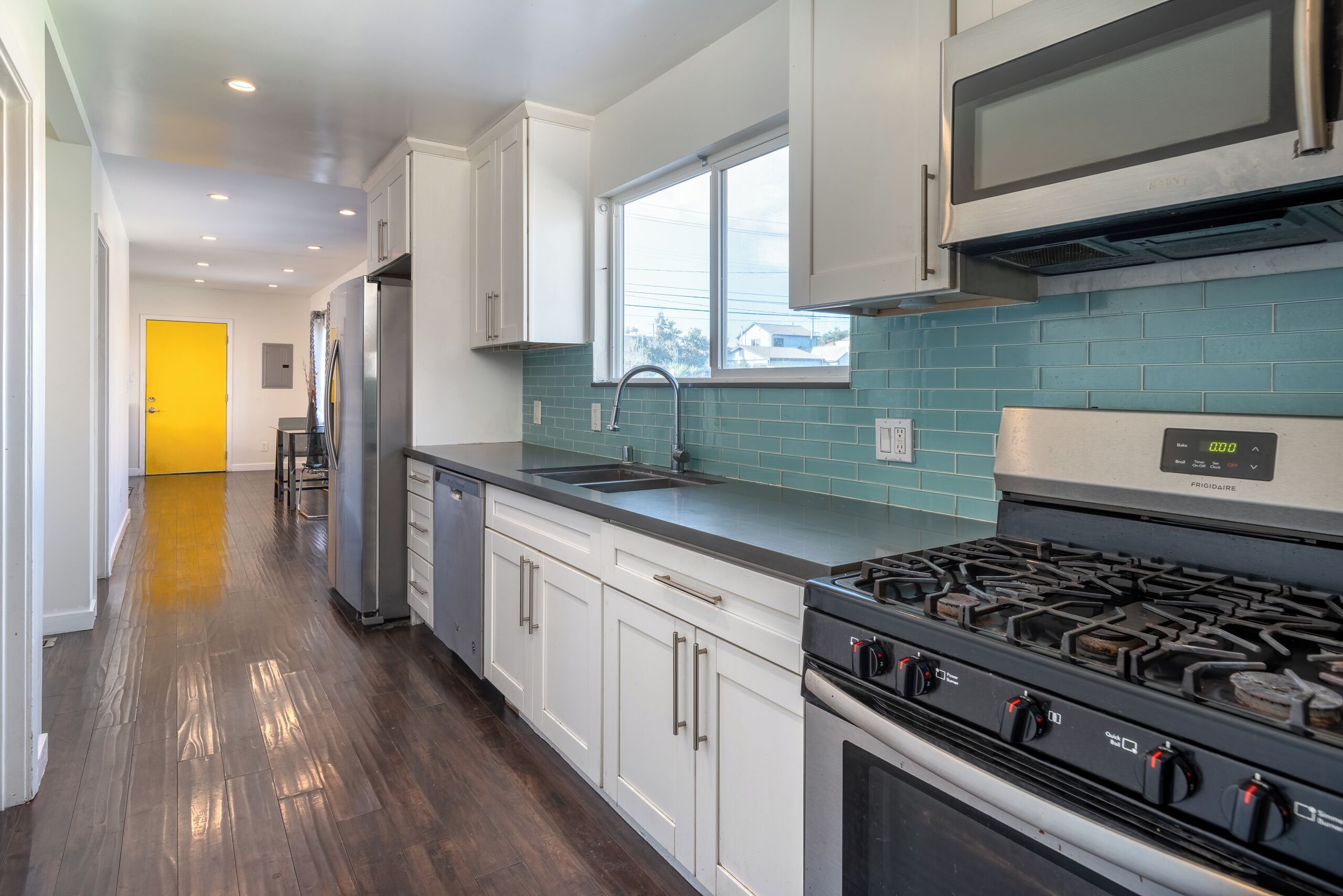 A modern kitchen with stainless steel appliances, a window, and teal backsplash.