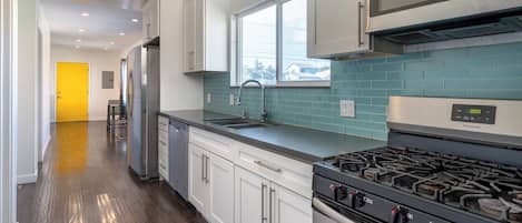 A modern kitchen with stainless steel appliances, a window, and teal backsplash.