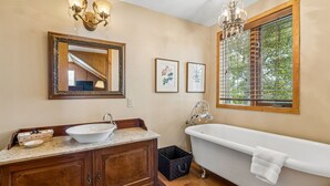 Ein Badezimmer mit freistehender Badewanne, einem Holzwaschtisch mit Waschbecken, einem großen Spiegel und gerahmten Pflanzenabbildungen an der Wand.