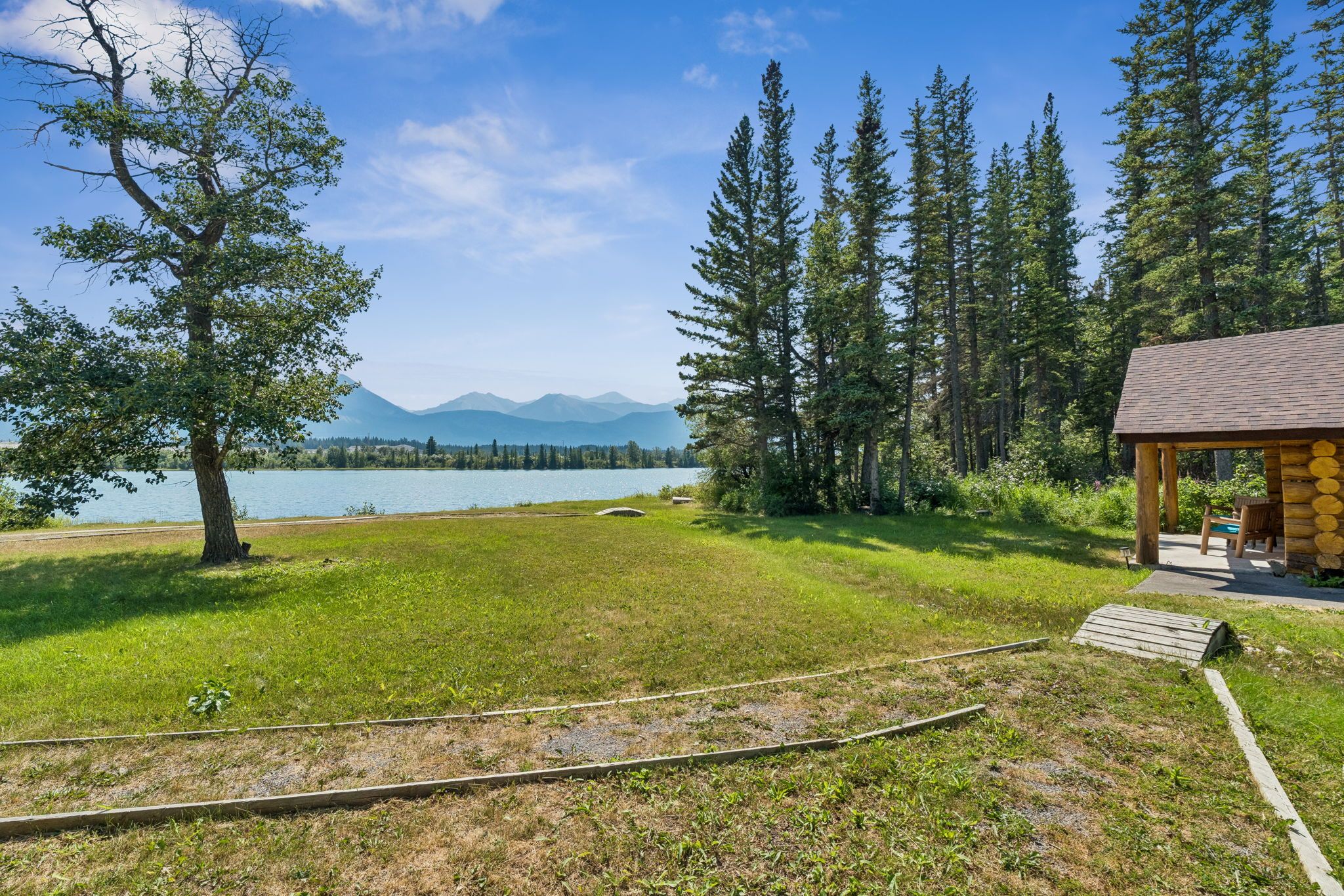 A grassy area with a wooden structure, a clear sky, and a lake with mountains in the background.