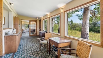 A hallway with a patterned carpet, wooden furniture, and large windows offering a view of trees and sky.