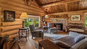 Ein gemütliches Holzblockhaus-Interieur mit Kamin, Holzmöbeln und gerahmten Bildern an den Wänden.
