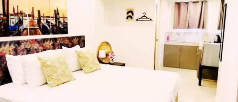 A hotel room with a bed, a bedside table, a mirror, a wall-mounted TV, and a door leading to a bathroom.
