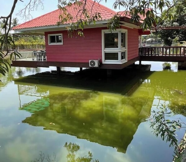 A house with a red roof and white trim, floating on water with a reflection visible.