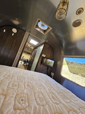 A bedroom with a bed, a television, and a window with a view of the outdoors.