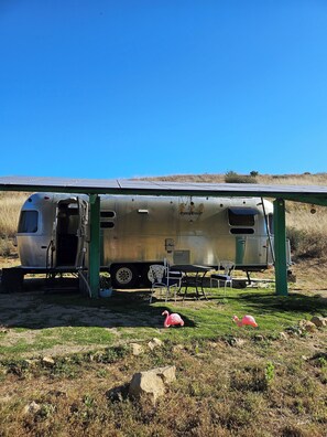 A stationary trailer with an open door, a table, and chairs underneath a solar panel.