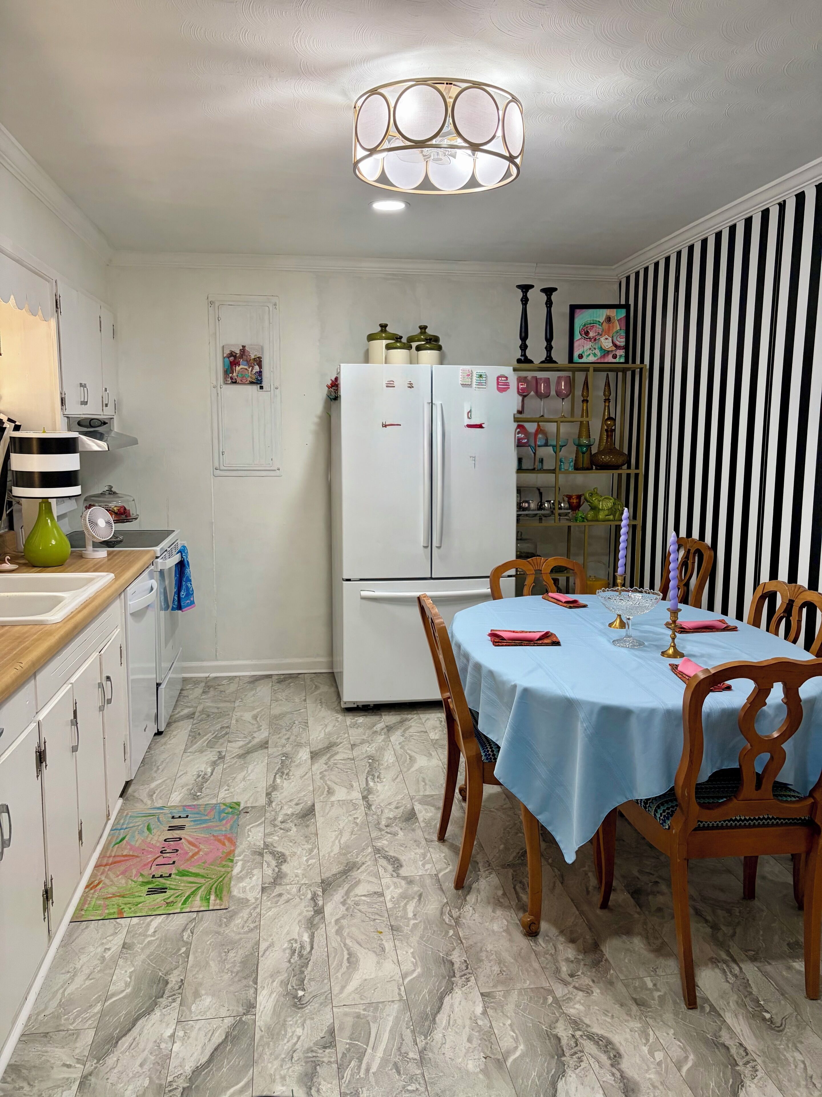 Una cocina con refrigerador blanco, una mesa de comedor con sillas, una lámpara colgante y una pared a rayas.
