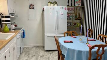 Una cocina con refrigerador blanco, una mesa de comedor con sillas, una lámpara colgante y una pared a rayas.
