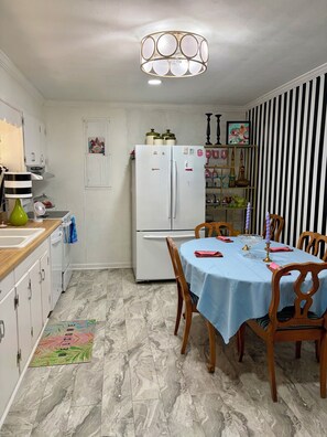 A kitchen with a white refrigerator, a dining table with chairs, a hanging light fixture, and a striped wall. - 3 bdr 1 bath home in Water Valley. Close to Oxford Ole Miss and Tri lakes area. (Water Valley)