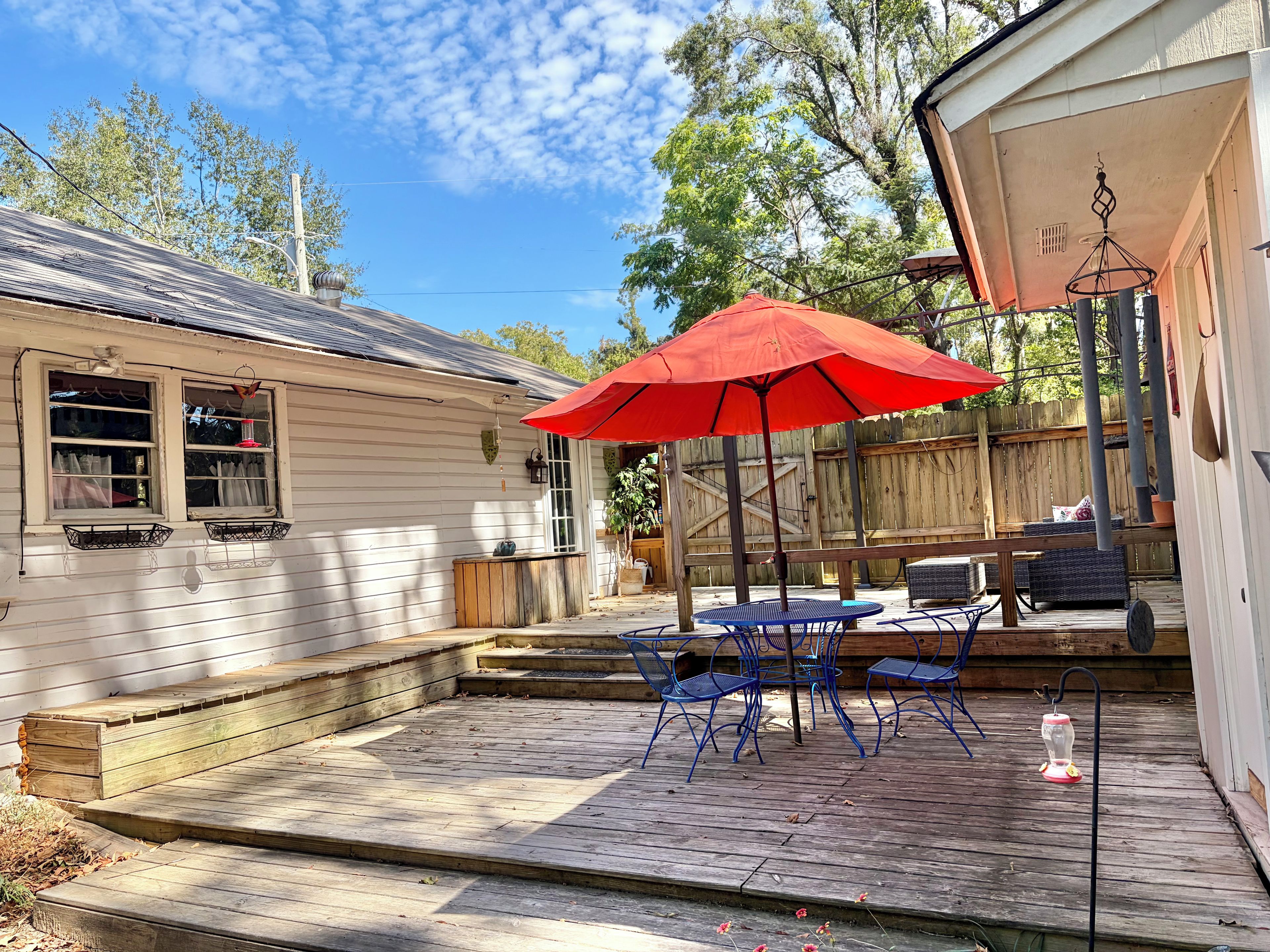 Eine Holzterrasse mit Tisch und Stühlen, einem roten Sonnenschirm und einem hängenden Laternen.