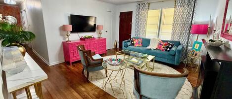 A living room with a television, a pink cabinet, a blue sofa, and a glass coffee table.