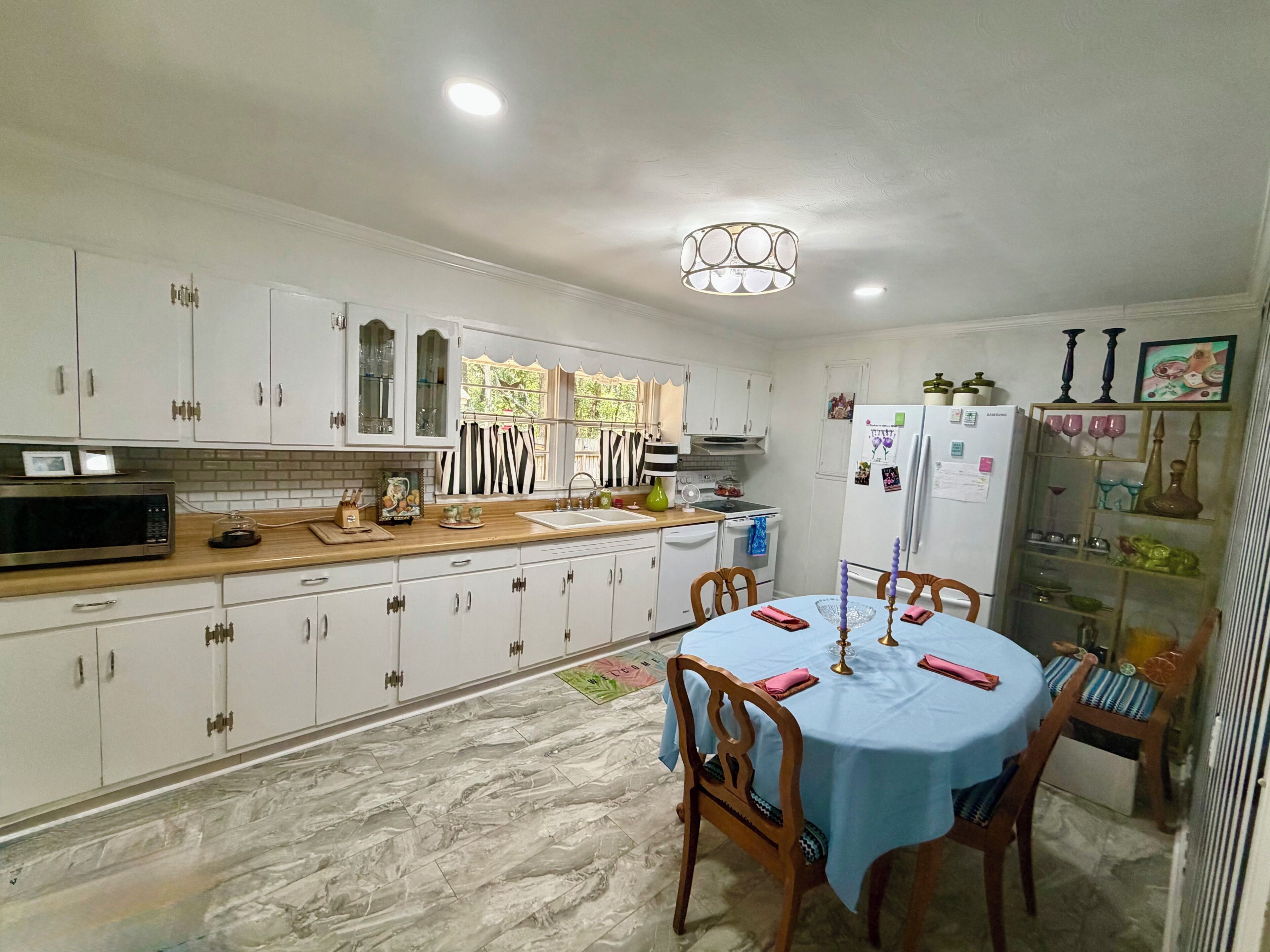 A kitchen with white cabinets, a microwave, a sink, and a dining area with a table set for two.