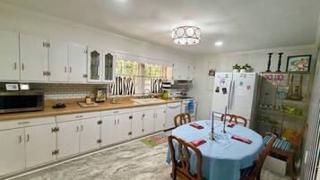 A kitchen with white cabinets, a microwave, a sink, and a dining area with a table set for two.