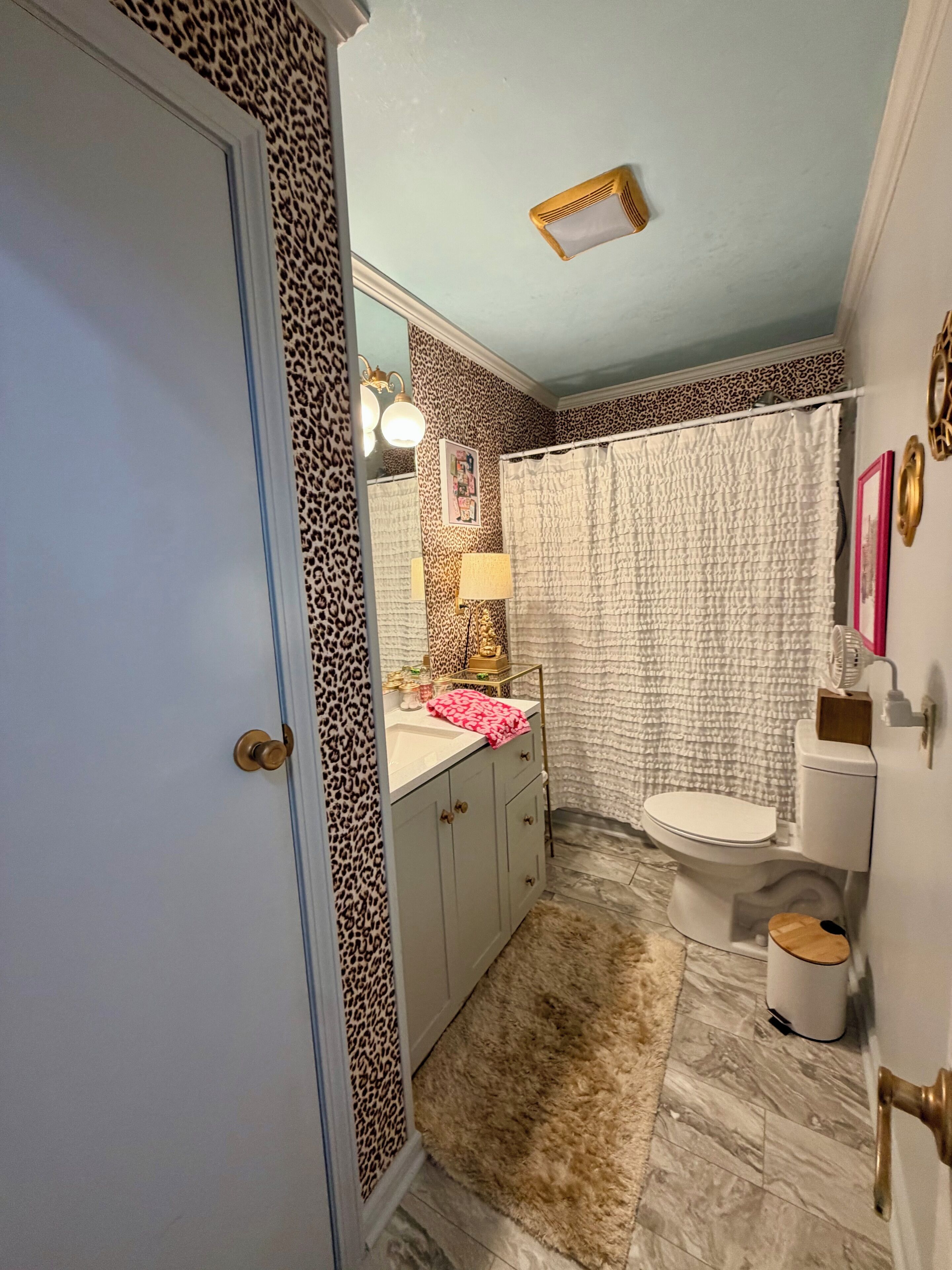 A bathroom with a leopard print wall, a white toilet, a sink with a pink towel, and a mirror.
