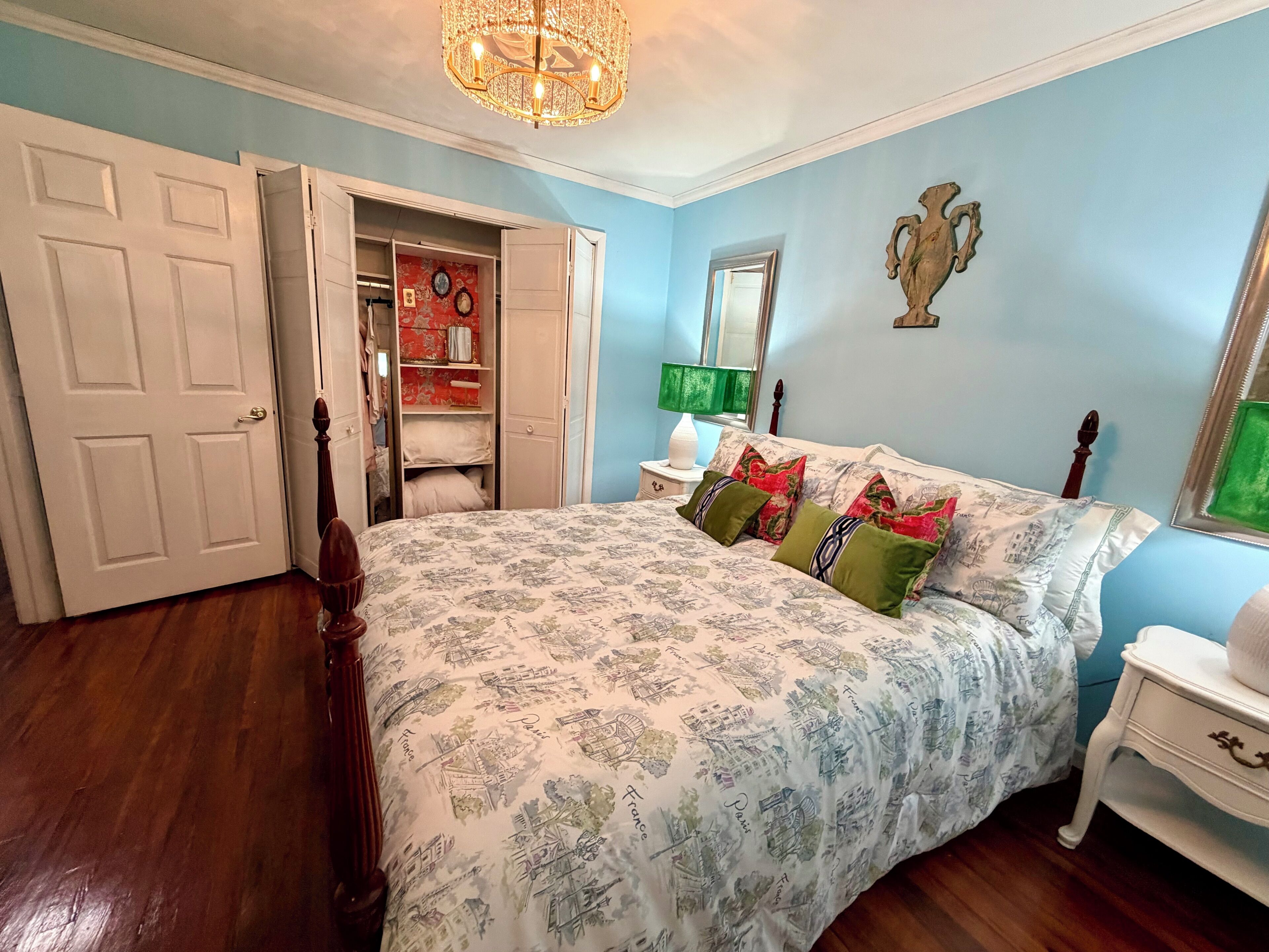 A bedroom with a bed, a wardrobe, a mirror, and a chandelier.