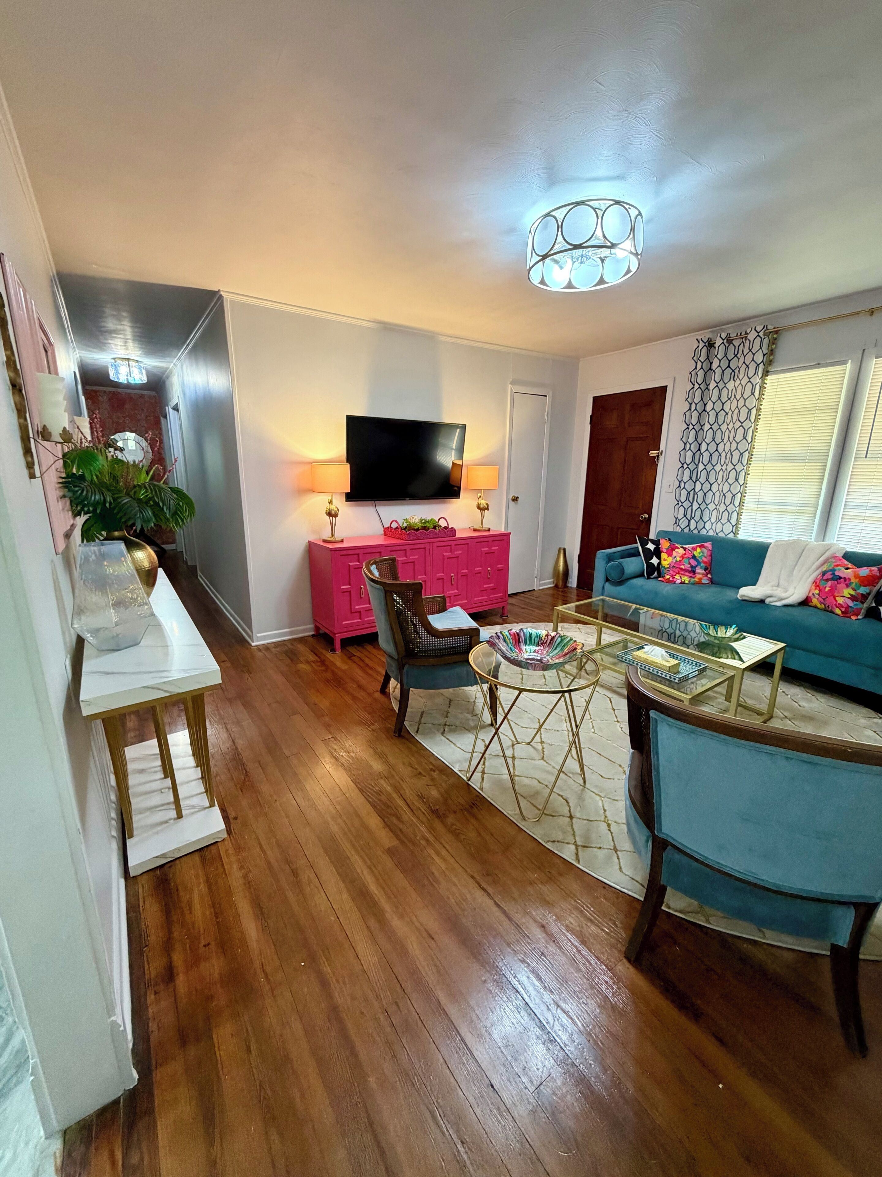 A living room with a flat-screen TV, a pink cabinet, a blue sofa, and a wooden floor.