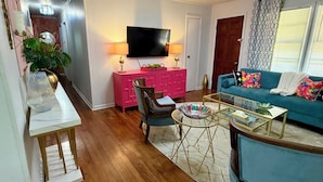 A living room with a flat-screen TV, a pink cabinet, a blue sofa, and a wooden floor.